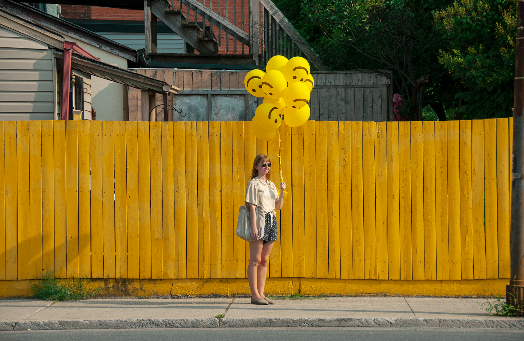 girl standing with yellow sarcastic emoji smile balloons
